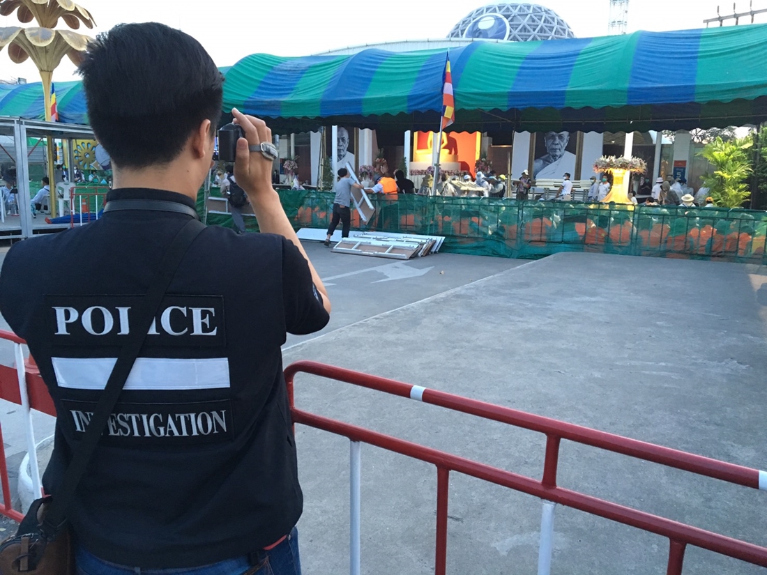 A policeman on Tuesday morning films supporters of Wat Dhammakaya inside tents and barricades at a gate of their temple complex.