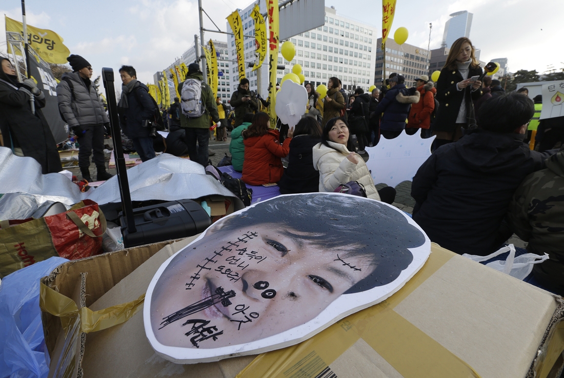 A defaced portrait of South Korean President Park Geun-hye is seen as protesters sit demanding the parliamentary impeachment of Park in front of the National Assembly in Seoul, South Korea, Friday, Dec. 9, 2016.(AP Photo/Ahn Young-joon)