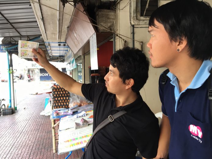 Two men check lottery tickets for authenticity Monday morning in Chanthaburi province.