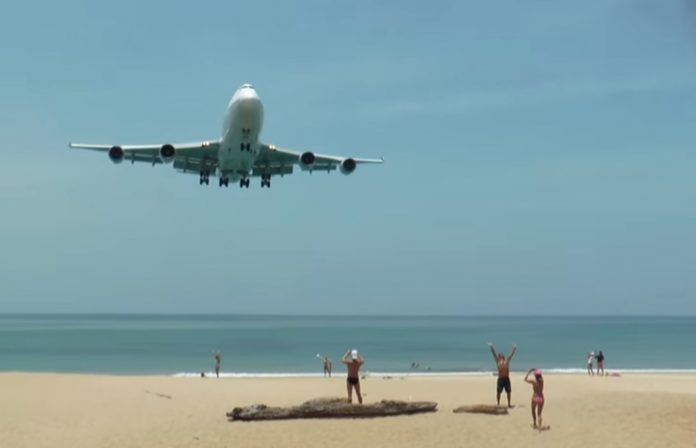 Tourists pose for photos as a jet approaches on March 21, 2016, at Phuket’s Mai Khao Beach.