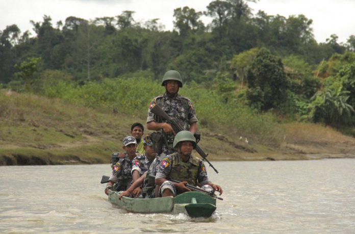 Myanmar Border Guard Police (BGP) officers travel in a wooden boat operated by Rohingya Muslim men in July at Tin May village in which Myanmar government and military claim the existence of alleged Muslim terrorists in Buthidaung, Rakhine State, Myanmar. Photo: Esther Htusan / Associated Press