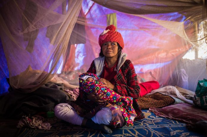 In a temporary shelter, a woman holds her newborn she delivered while fleeing violence in Myanmar’s Kachin state. Photo: Hkun Lat / Facebook