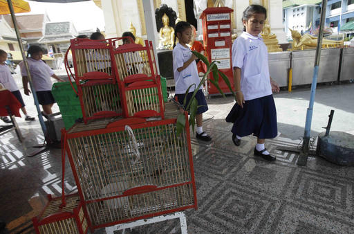 Students walk past caged birds sold to be released for good luck at the Wat Trimitr on Friday in Bangkok Photo: Sakchai Lalit / Associated Press