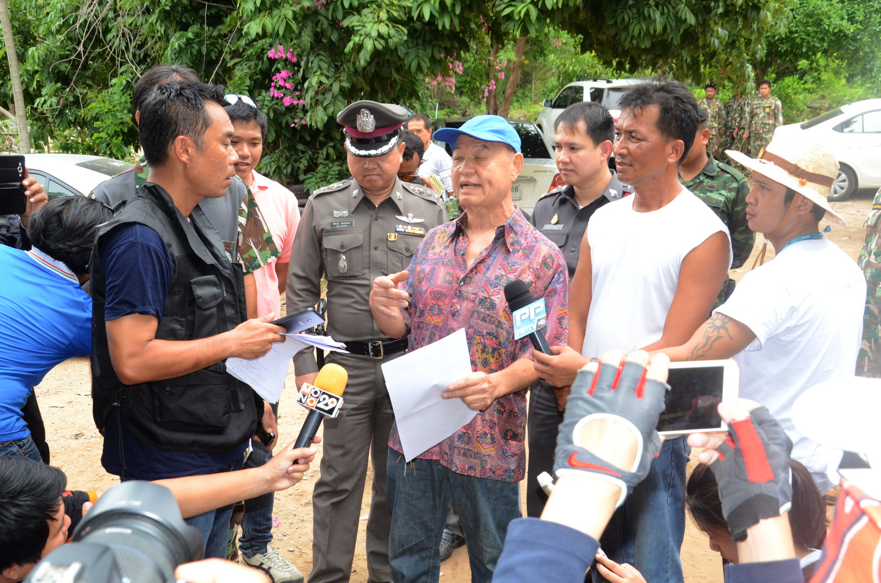 Thawat Kajornchaikul, also known as Sia Tong, in blue cap, speaks to officers and the media Wednesday afternoon outside his house in Kanchanaburi city.