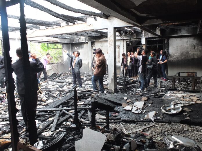 Interim parliament member Tuang Untachai points as photographers snap photos Tuesday in the burned dormitory of Chiang Rai’s Pitakkiet Witthaya School. Numerous VIPs have visited the school and posed for photo-ops since the fire, but no legal action has been taken.
