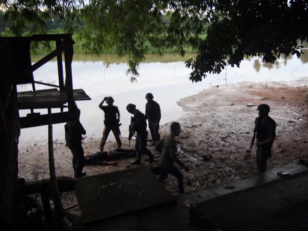 Police commandos surround Piya’s body after shooting his fingers off Tuesday.