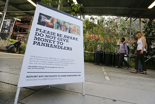 Pedestrians pass a warning sign about panhandlers dressed as monks at The High Line, one of New York City's most visited attractions. They wear orange robes and carry shiny medallions, stopping people in New York City to offer greetings of peace. The men identify themselves as Buddhist monks and solicit donations for a temple in Thailand. Photo: Frank Franklin II / Associated Press