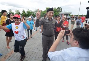 An amused police officer poses for photos before dancing protesters Wednesday outside Election Commission offices at the Chaeng Wattana Government Complex in Bangkok.