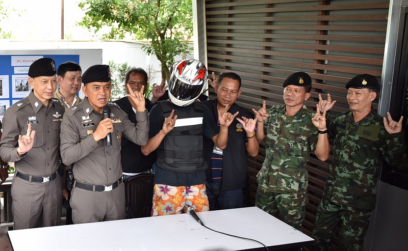 Bangkok Police Chief Sanit Mahatavorn, third from left, demonstrates the ‘ILY’ sign Wednesday in Bangkok along with police, military officers and an 18-year-old vocational student accused of murdering a rival, in helmet.