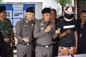 Bangkok Police Chief Sanit Mahatavorn, third from left, shows an 18-year-old murder suspet, in helmet, how to make a 'mini-heart' with his hand Wednesday in Bangkok.