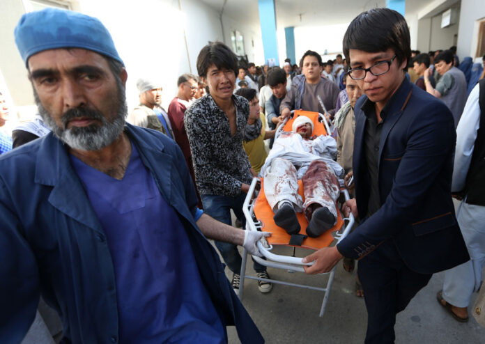 Afghans help a man injured in a deadly explosion Saturday that struck a protest march by ethnic Hazaras in Kabul, Afghanistan. Photo: Rahmat Gul / Associated Press