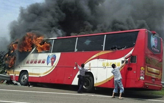 A policeman and another man try to break the windows of a burning tour bus on the side of a highway in Taoyuan, Taiwan, on Tuesday. Photo: Yan Cheng / Scoop Commune / Associated Press