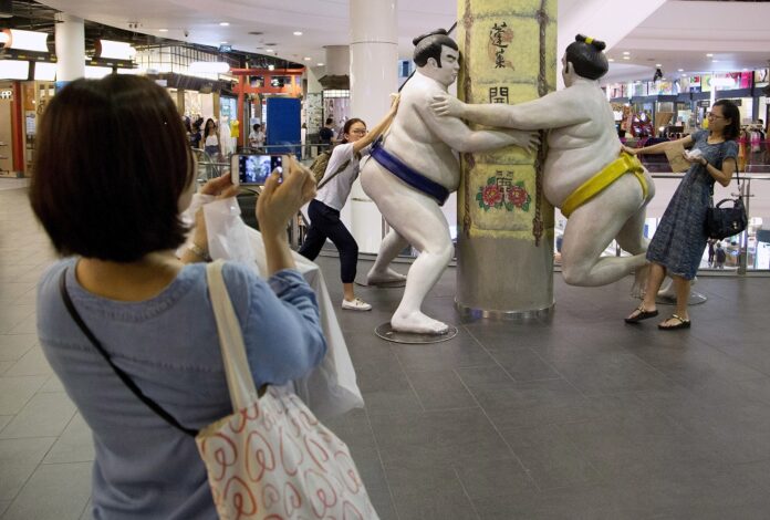 Shoppers pose for a photo with sumo wrestler statues on a Japanese themed floor of a major shopping mall in central Bangkok, Thailand. Photo: Mark Baker / Associated Press