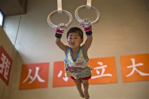 In this photo taken Thursday, June 16, 2016, a young child practices on still rings at the Xuhui Sports School near the slogans "Set ambitious goals from young" in Shanghai, China. Photo: Associated Press