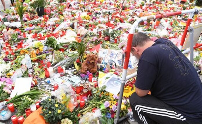 A man prays next to flowers and candles that have been placed in front of the main entrance of the Olympia-Einkaufszentrum (Olympia Shopping Mall) in Munich, Germany, Monday, July 25, 2016, after a rampage that left numerous people dead and injured. Photo: Peter Kneffel