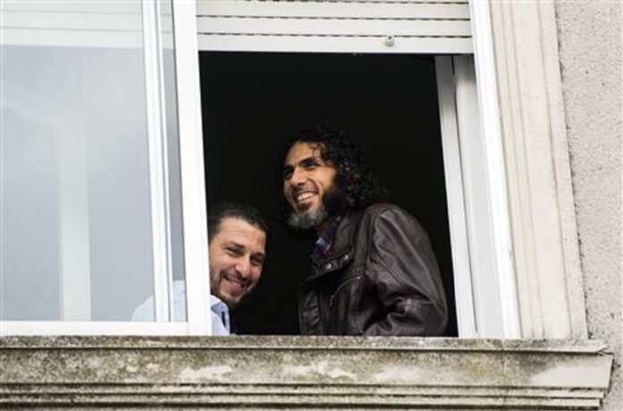 In this June 5, 2015 file photo, Abu Wa'el Dhiab, from Syria, right, and Adel bin Muhammad El Ouerghi, of Tunisia, both freed Guantanamo Bay detainees, stand next to the window of their shared home in Montevideo, Uruguay