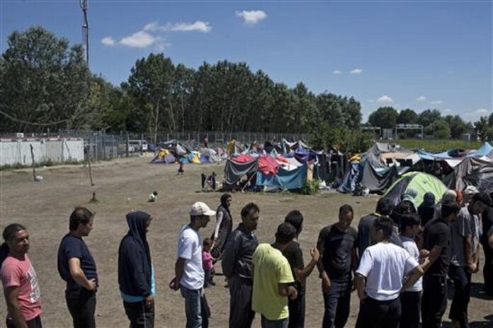 People queue to receive aid packages at a makeshift migrant and refugee camp situated meters away from the Serbian border with Hungary, in Horgos, Serbia, Monday, July 4, 2016.