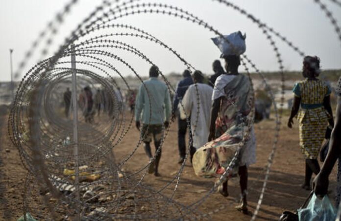 In this photo taken Tuesday, Jan. 19, 2016, displaced people walk next to a razor wire fence at the United Nations base in the capital Juba, South Sudan. Photo: Jason Patinkin