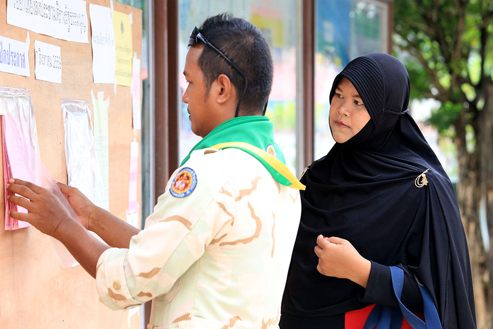 A paramilitary ranger and civilian woman check the rolls at a polling station Sunday in Yala province.