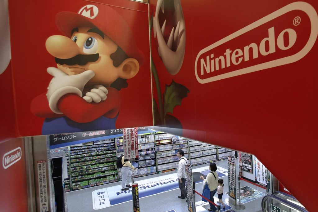 In this May 7, 2014, file photo, shoppers walk under the logo of Nintendo and Super Mario character, left, at an electronics store in Tokyo.