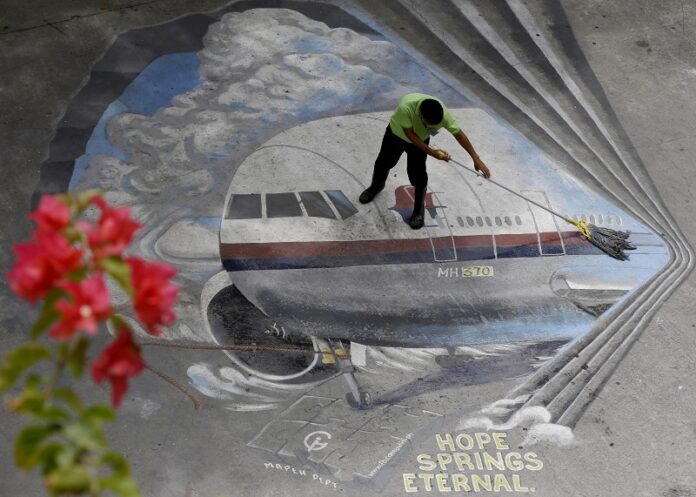 A school utility worker mops a mural depicting the missing Malaysia Airlines Flight 370 at the Benigno