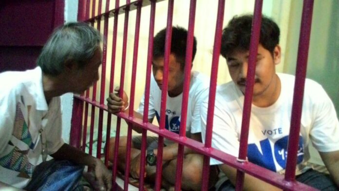 Wiboon Boonpattararaksa talks to his son Jatupat Boonpattararaksa, at center, on Aug. 6 at a police station holding cell in Chaiyaphum province. Jatupat was on a hunger strike to protest his arrest for campaigning against the charter. Photo: Thai Lawyer for Human Rights