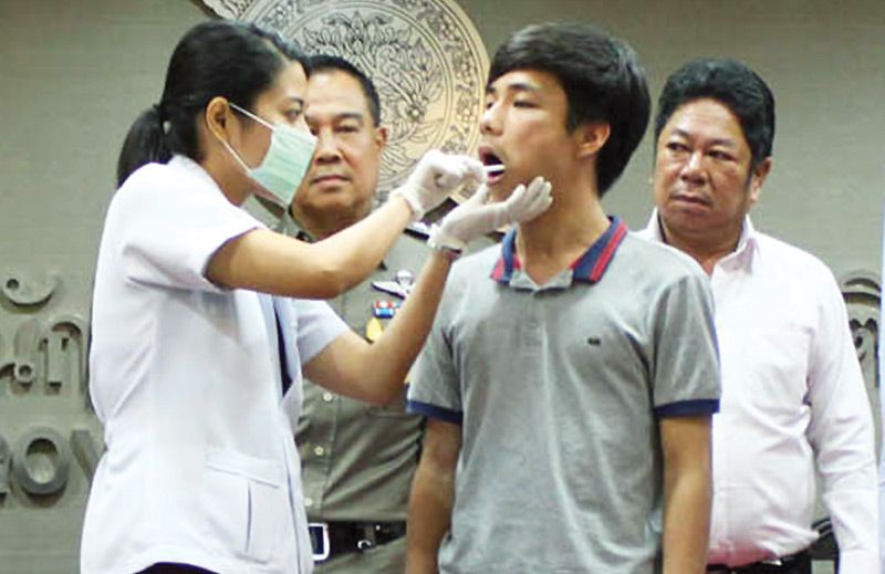 A forensic police officer tests Warot Toovichien for DNA on Oct. 30, 2014, while his father Woraphan Toovichien, at right, looks on at Royal Thai Police headquarters in Bangkok.