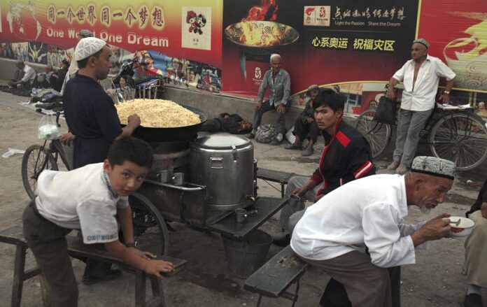 Uighurs rest near a food stalls and Beijing Olympic Games billboards in 2008 in China's western Xinjiang province. Photo: Ng Han Guan / Associated Press