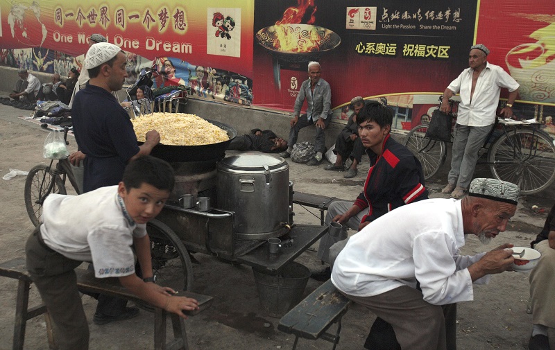 Uighurs rest near a food stalls and Beijing Olympic Games billboards in 2008 in China's western Xinjiang province. Photo: Ng Han Guan / Associated Press