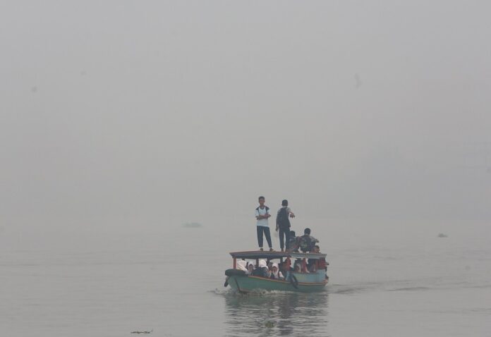 students ride on a boat on their way to school Thursday while haze from wildfires blanket the Musi River in Palembang, South Sumatra, Indonesia. Photo: Tatan Syuflana / Associated Press
