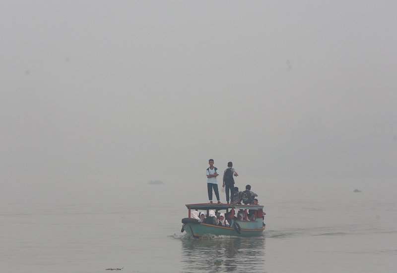 students ride on a boat on their way to school Thursday while haze from wildfires blanket the Musi River in Palembang, South Sumatra, Indonesia. Photo: Tatan Syuflana / Associated Press