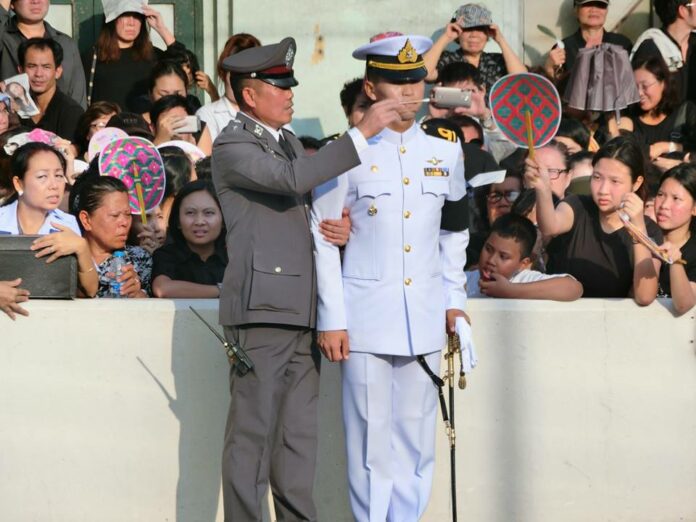 A policeman waves smelling salts before a naval officer who nearly fainted Friday as he stood guard for the royal funerary procession in Bangkok. Photo: Prueksachat Cherdchai / Facebook
