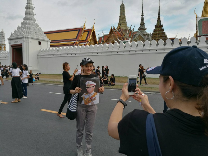 A woman poses for a photo holding a photograph of His Majesty the Late King on Thursday in Bangkok.