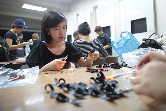 Volunteers at Thammasat University’s Tha Prachan campus on Sunday make black ribbons to be given away for free in the Sanam Luang.