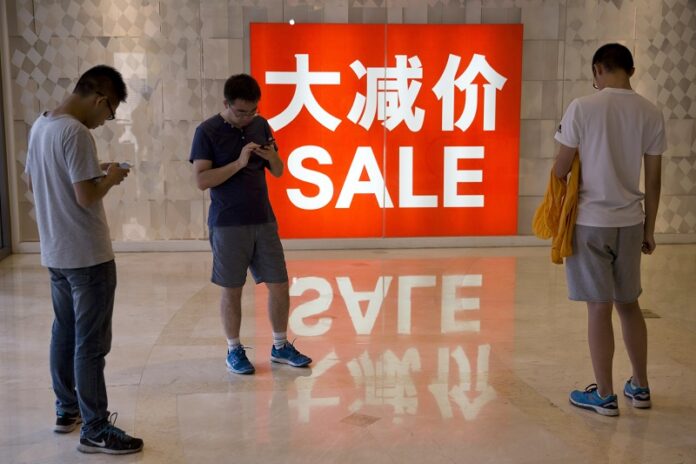 Chinese shoppers stand near a sale advertisement on July 10, 2016, at a shopping area in Beijing. Photo: Ng Han Guan / Associated Press