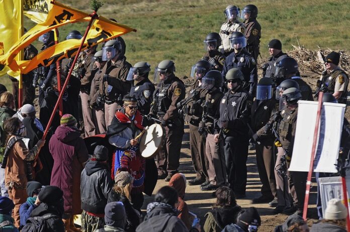 A person with a hand drum paces between law enforcement officers and a line of protesters Monday along North Dakota Highway 6, south of St. Anthony, North Dakota. Photo: Tom Stromme / Associated Press