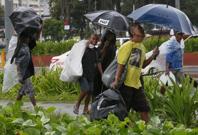 Residents walk with bags of plastics bottles and other reusable materials under a slight rain brought about by Typhoon Sarika Sunday in Manila, Philippines. Photo: Bullit Marquez / Associated Press
