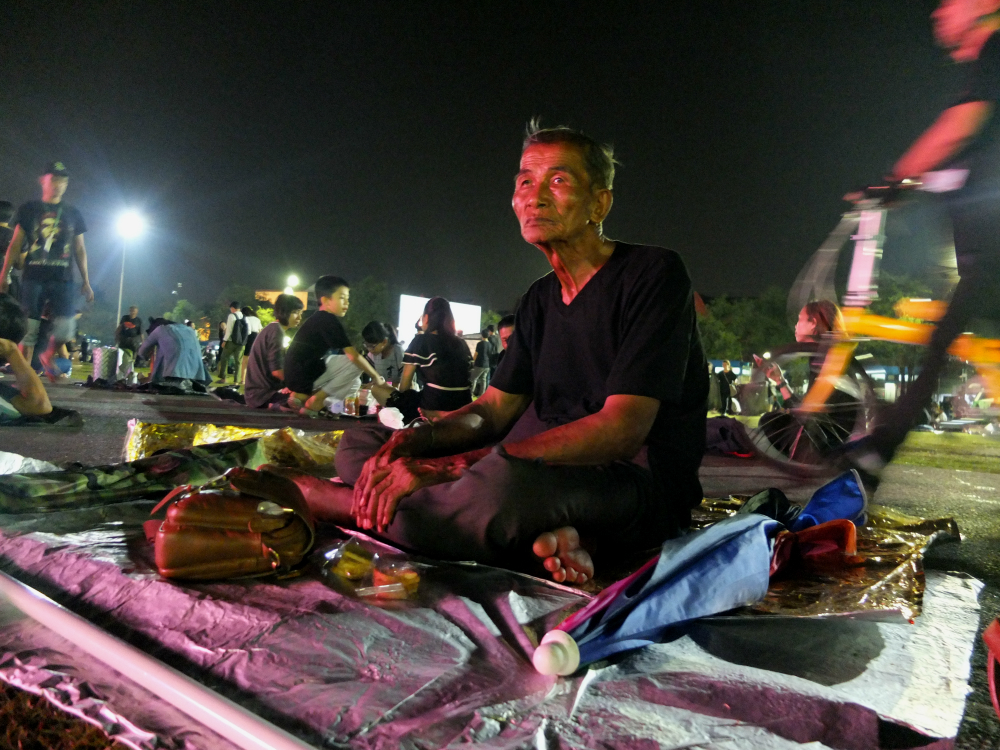 Phrom Onsri sits on a mat Wednesday at Sanam Luang with his big umbrella and portable camping tent.