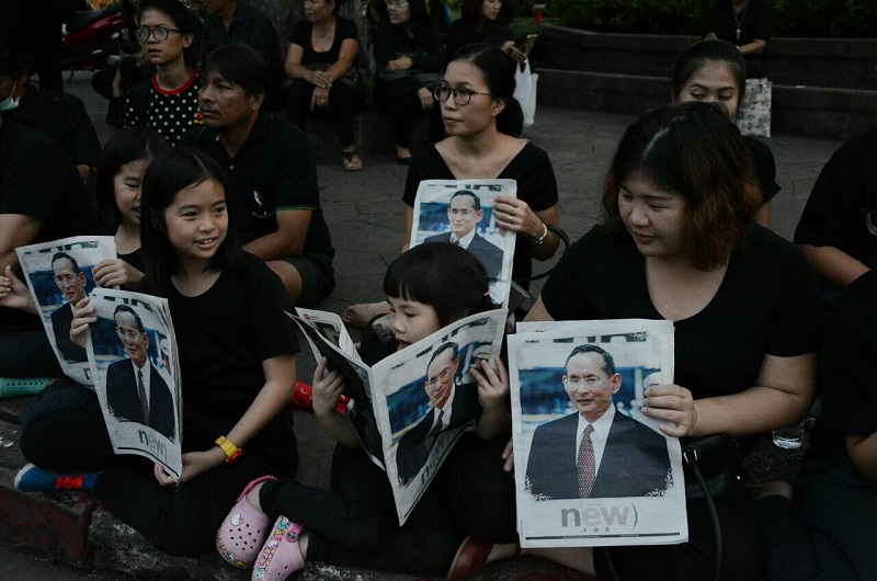 Mourners hold magazines with photos of the King Tuesday evening at the Grand Palace in Bangkok.