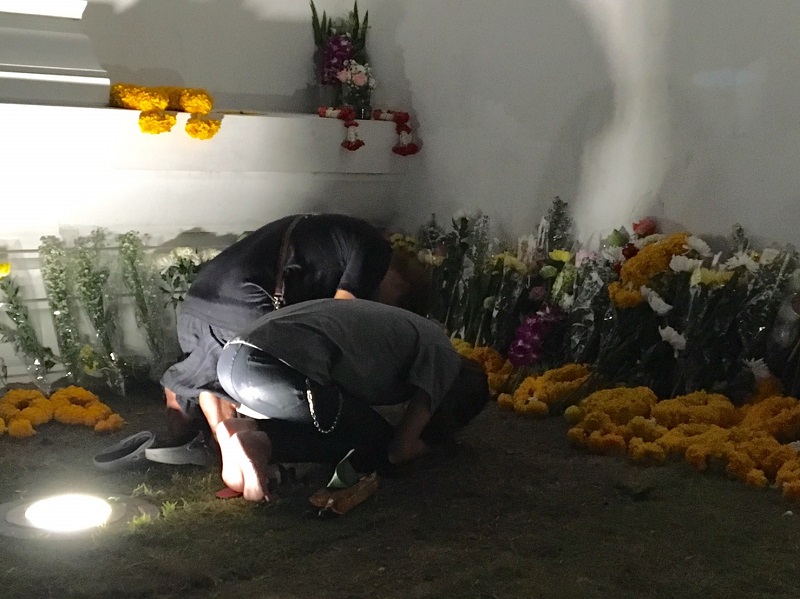 Mourners offer marigold garlands and lotuses and prostrate themselves Tuesday at the palace wall.