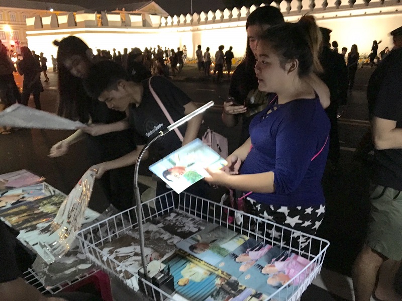 Mourners Tuesday night purchase posters and photos of His Majesty the Late King near the Grand Palace.