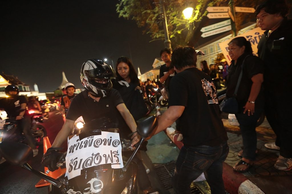 A man offers free motorcycles rides Sunday at Sanam Luang . On his motorcycle a sign reading: “For dad, free transport.”