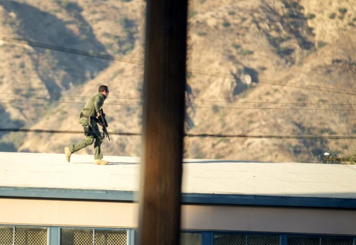A SWAT team sniper moves on top of the Memorial Park gymnasium to cover a barricaded suspect Tuesday on Fourth Street east of Orange Avenue after several people were shot at that location Avenue in Azusa, California. Photo: Leo Jarzomb / Associated Press