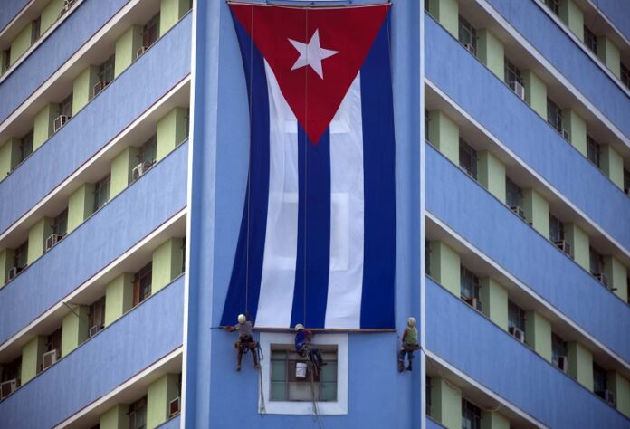 Workers on Sunday hang a giant Cuban flag on a government building in Havana, Cuba, two days after the death of Fidel Castro. Cuba is observing nine days of mourning for the former president who ruled Cuba for half a century. Photo: Ramon Espinosa / Associated Press