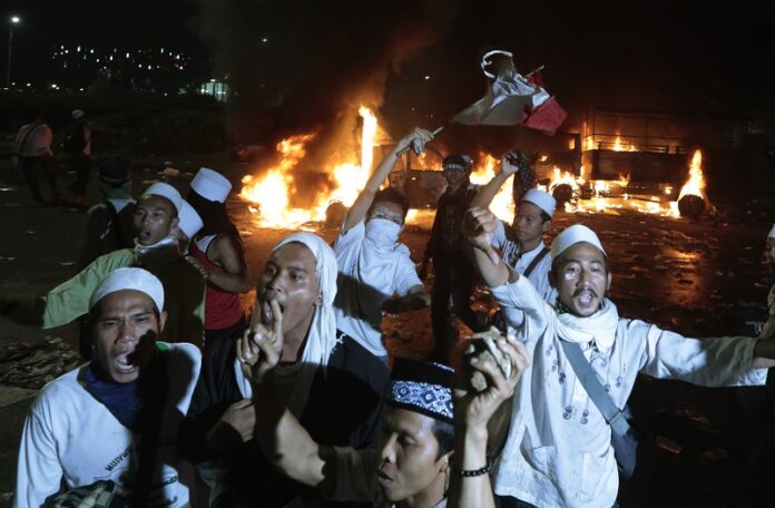 Muslim protesters chant slogans Friday near burning police trucks during a clash with the police outside the presidential palace in Jakarta, Indonesia. Photo: Dita Alangkara / Associated Press