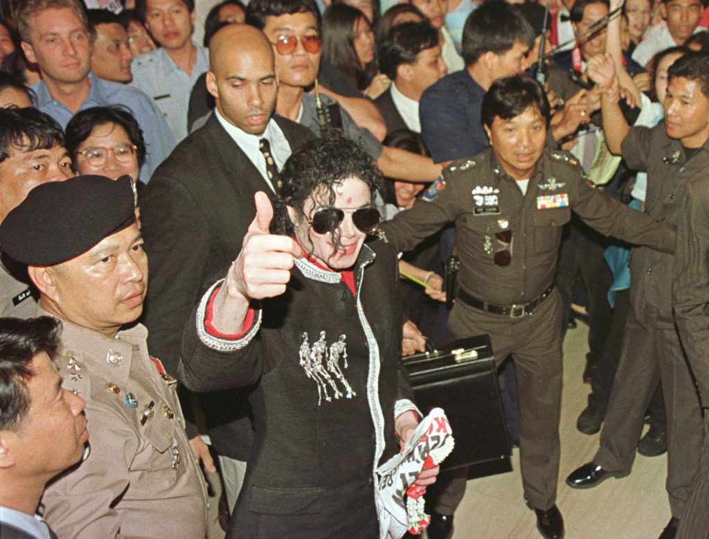 Michael Jackson on Nov. 2, 1996, gives a thumbs up to fans and cameras while being accompanied by officers at a hotel in Bangkok. Photo: Charles Dharapak / Associated Press