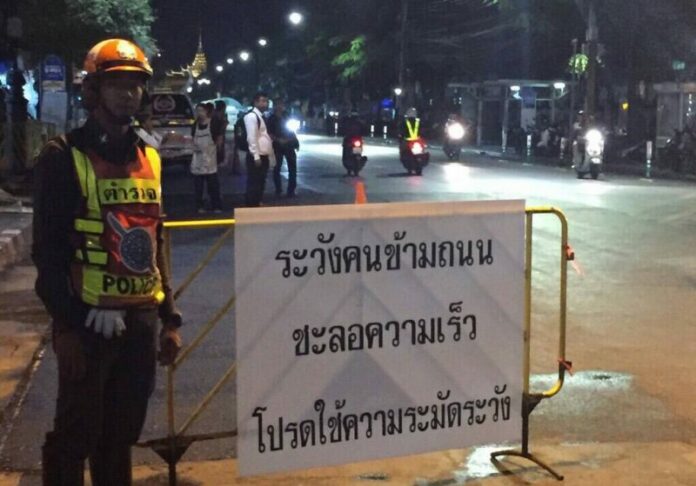 Traffic police officer with a sign asking people to slow down and watch out for pedestrians at a road near Sanam Luang.