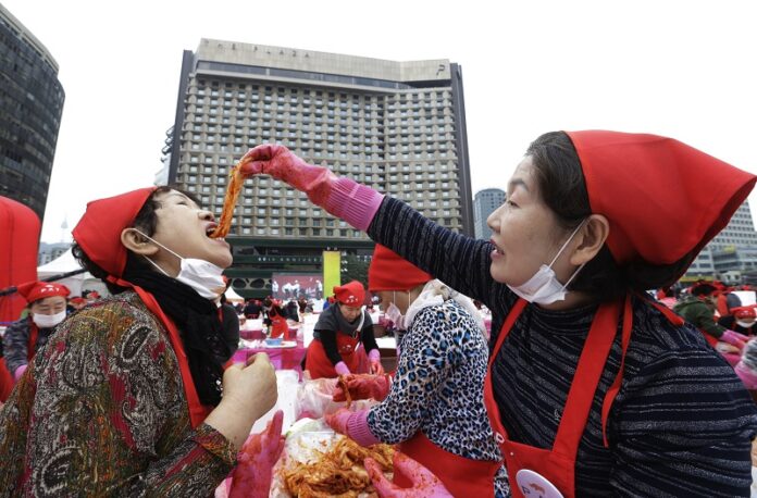 Volunteer Kim Yeon-sook, left, tastes kimchi, Korean pickled vegetables, from her colleague Lee Hyun-sook as they make it to donate to needy neighbors for winter preparation on Friday during the Seoul kimchi festival in Seoul, South Korea. Photo: Ahn Young-joon / Associated Press