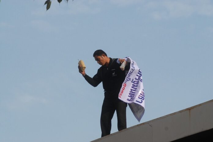 Chalerm Sornnonthee stands atop a bank near the Government House, wielding what police would later say was in fact not a large bomb on Tuesday in Bangkok.