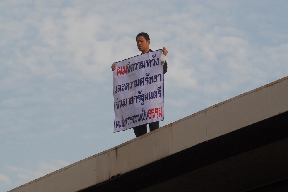 Chalerm Sornnonthee stands atop a bank near the Government House, wielding what police would later say was in fact not a large bomb on Tuesday in Bangkok.